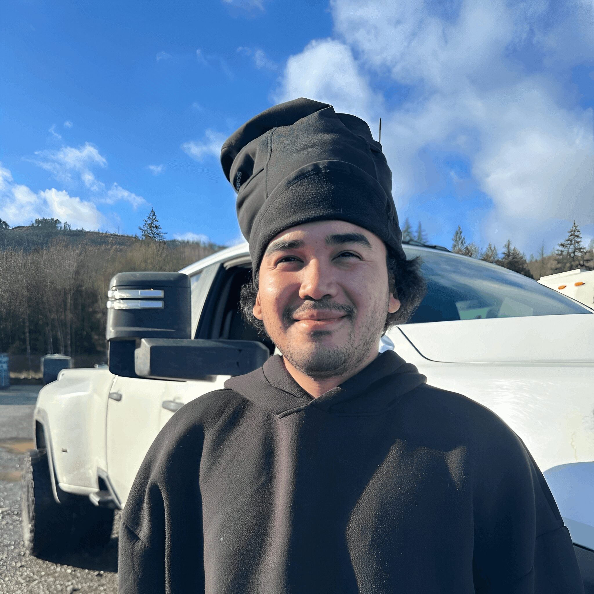 Smiling person in black hoodie near truck.