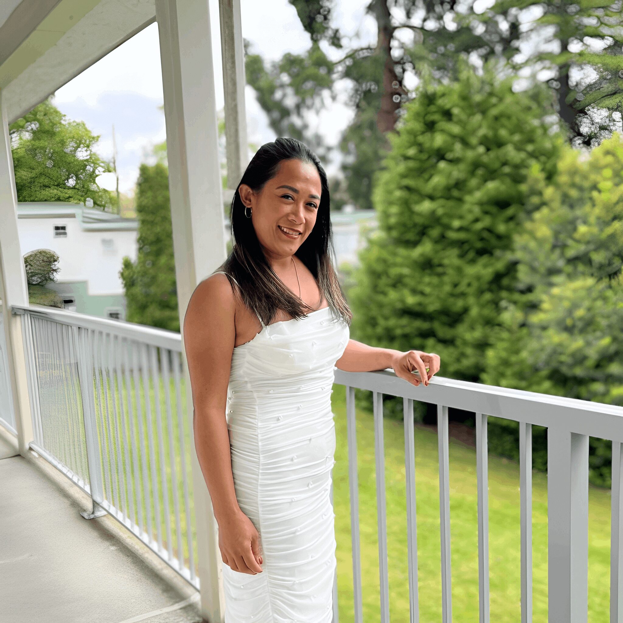 Smiling woman in white dress on balcony.