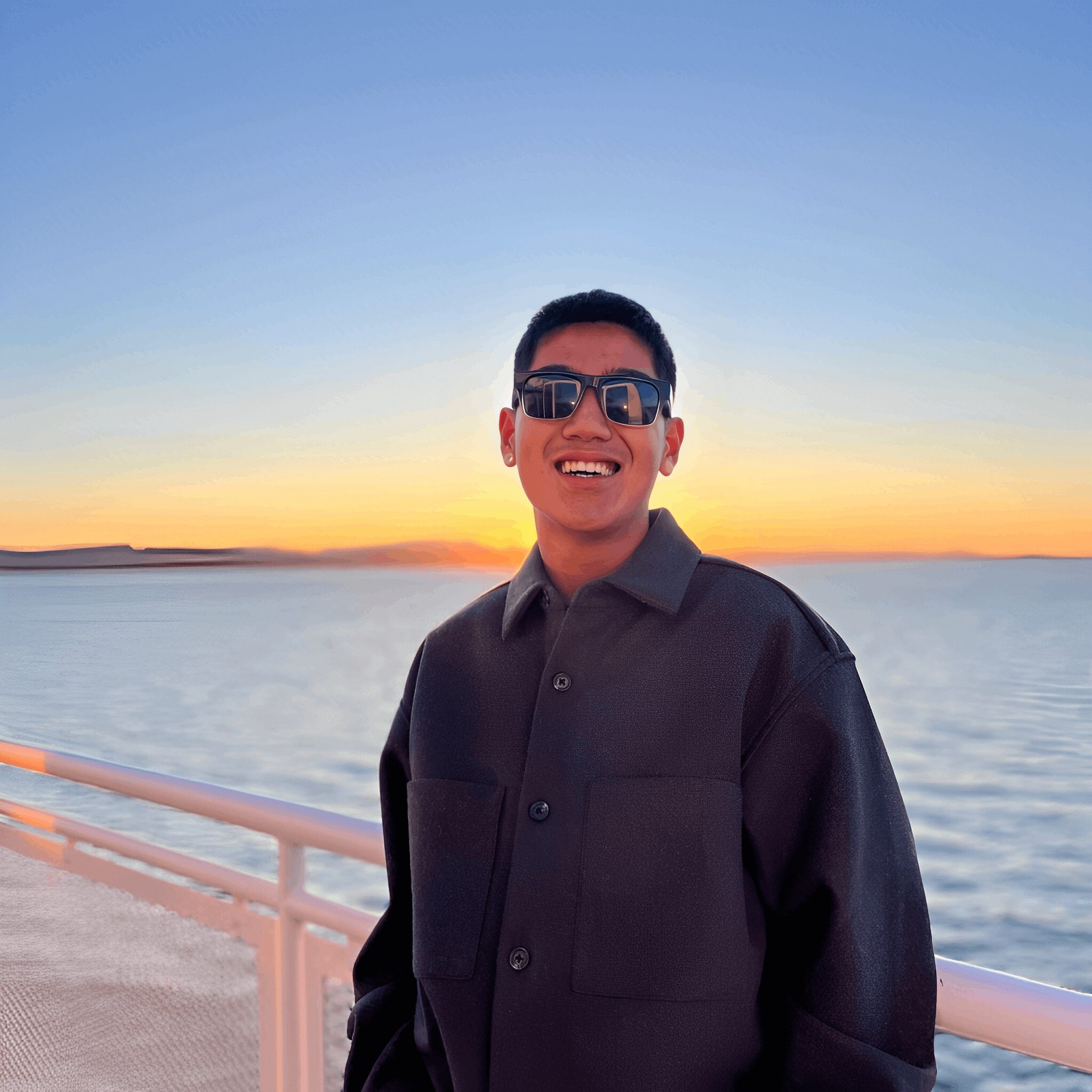 Smiling person wearing sunglasses at sunset.