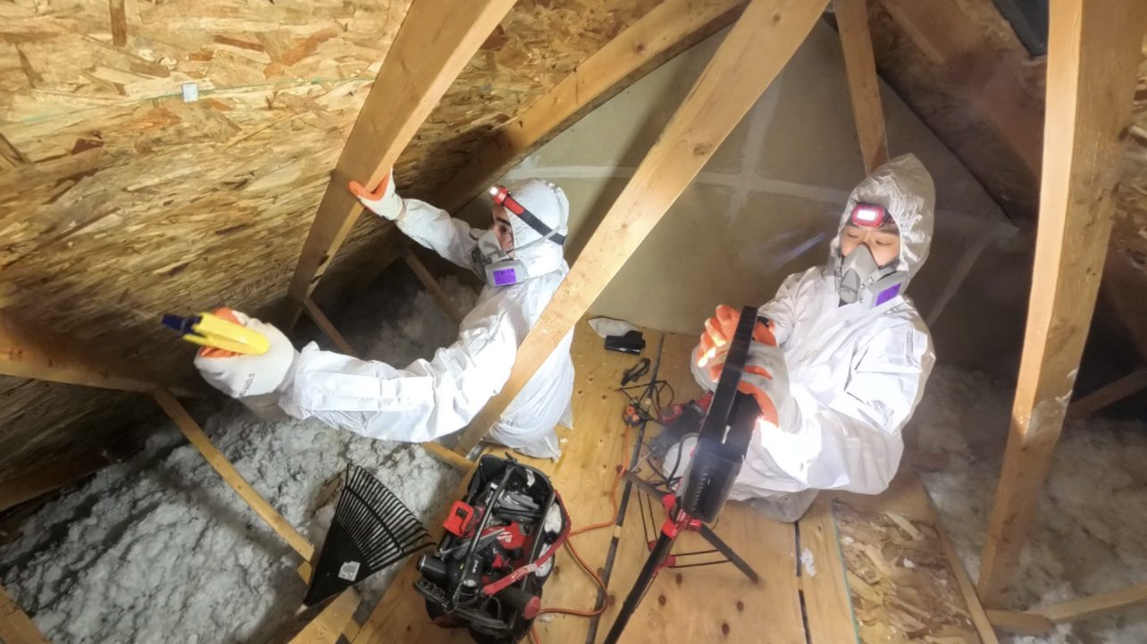 A man in white suit working on the inside of an attic.